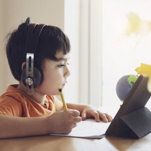 Portrait of preschool kid using tablet for his homework, Soft focus of Child wearing head phone doing homework by using digital tablet searching information on internet, Home schooling education concept,self isolation or Social Distancing